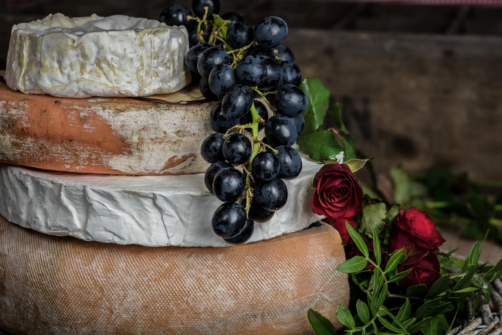 Stacked wheels of cheese with black grapes and roses